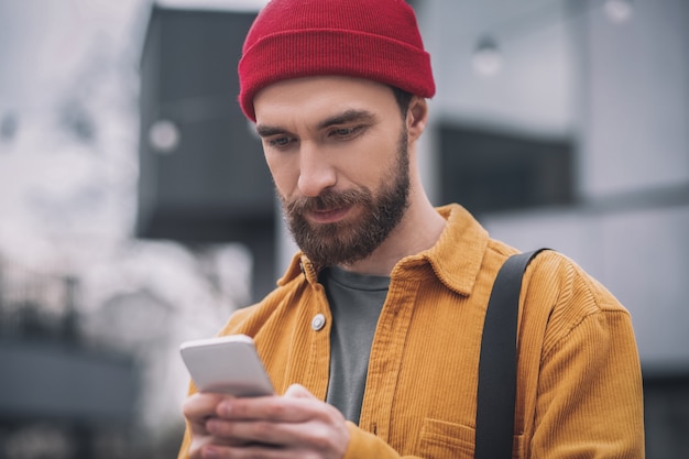 Online. Mężczyzna w czerwonym kapeluszu, trzymając telefon i wysyłając SMS-a