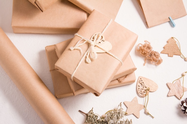 Zdjęcie opakowania prezentów świątecznych w stylu ekologicznym, niektóre pudełka na prezenty ozdobione drewnianymi zabawkami na choinkę, sucha gałąź świerkowa, białe tło, styl życia zero odpadów
