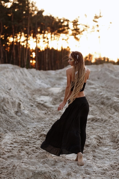 Opalona dziewczyna z dredami w czarnej spódnicy o zachodzie słońca na plaży
