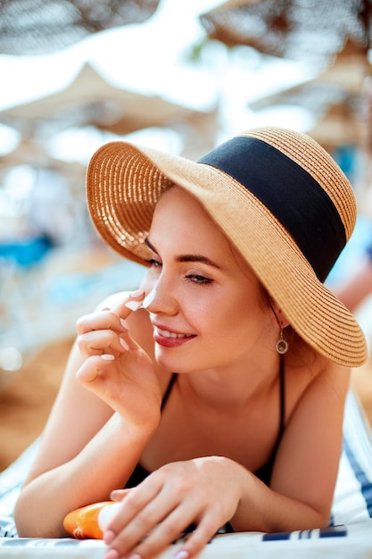 Opalona kobieta w kapeluszu stosująca krem przeciwsłoneczny z filtrem słonecznym Piękna szczęśliwa kobieta rozmazuje balsam z kremem do opalania