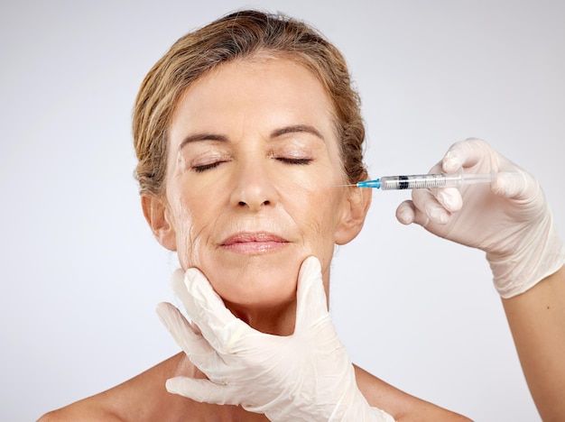 Operacja botoksu i twarz z dojrzałą kobietą otrzymującą zastrzyk w policzek w celu pielęgnacji urody i medycyny w studio na niebieskim tle Produkt wypełniający i kosmetyki z modelką w środku