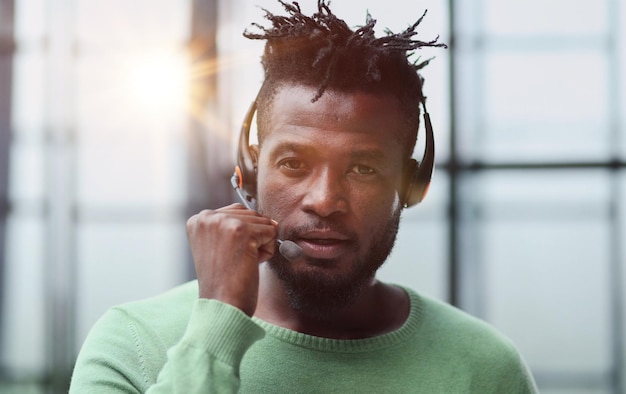 Operator gorącej linii Portret wesołego afrykańskiego przedstawiciela obsługi klienta z zestawem słuchawkowym w pustym miejscu w centrum telefonicznym