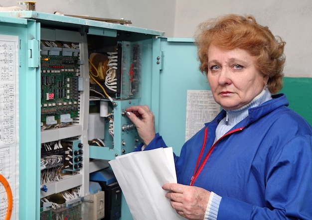 Operator kobieta-inżynier w maszynowni (winda) w pobliżu szafki elektronicznej.