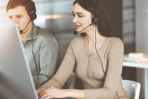 Operatorzy call center w pracy. Dwóch młodych ludzi w słuchawkach rozmawia z klientami, siedząc w słonecznym biurze.