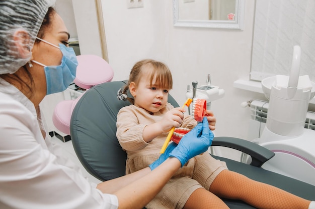 Opieka dentystyczna. Dentysta z małym pacjentem uczącym się mycia zębów na protezie.