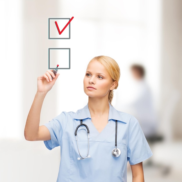 opieka zdrowotna, medycyna i technologia - młody lekarz lub pielęgniarka z markerem rysującym czerwony znacznik wyboru w polu wyboru