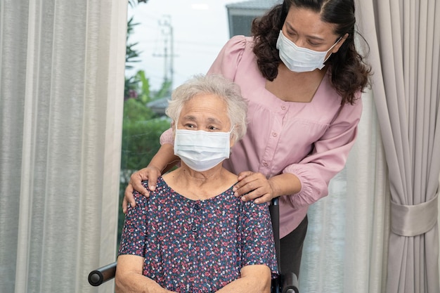 Opiekun pomaga Azjatycka starsza lub starsza starsza kobieta siedząca na wózku inwalidzkim i nosząca maskę na twarz w celu ochrony przed infekcją Covid19 Koronawirus