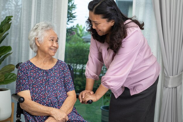 Opiekun pomaga azjatyckiej starszej kobiecie na wózku inwalidzkim z miłością w domu