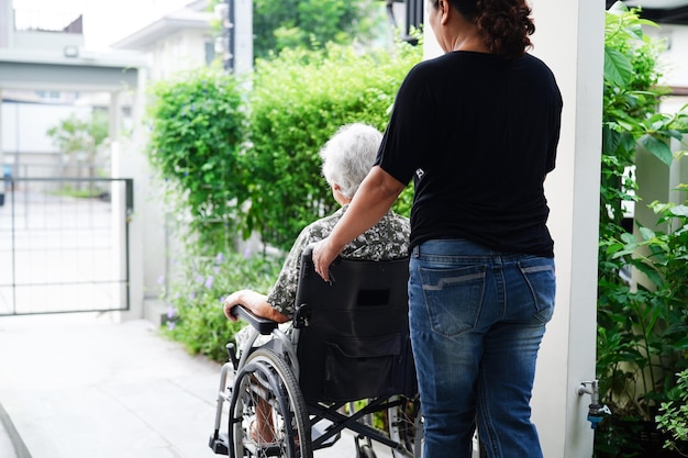 Opiekun pomaga azjatyckiej starszej kobiecie niepełnosprawnej pacjentce siedzącej na wózku inwalidzkim w szpitalnej koncepcji medycznej