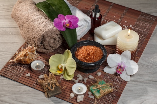 Oprawa spa i wellness z kwiatami orchidei, miska z solą morską, muszla, butelka z aromatycznym olejkiem, mydło, świece i ręczniki na bambusowej serwetce