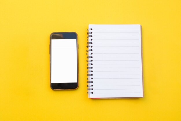 Opróżnia papier notatnik i mądrze telefon na żółtym tle