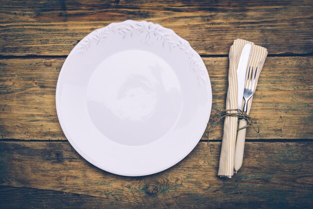 Opróżnij talerz na starym drewnianym stole z nożem, widelcem i serwetką