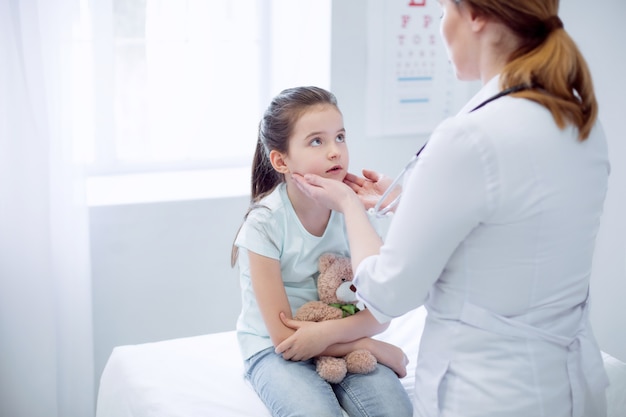 Opuchnięte migdałki. Młoda zamyślona dziewczyna siedzi patrząc na lekarkę, która testuje jej migdałki
