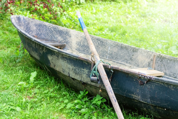 Zdjęcie opuszczona stara łódź wiosłowa z wiosłem na zielonej trawie pod drzewem nad rzeką lub jeziorem