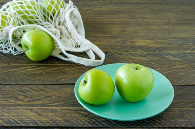 Organiczne jabłka Granny Smith na talerzu z siatkową torbą tekstylną na drewnianym stole.