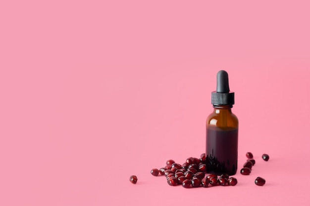 Organiczny kosmetyczny olej z pestek granatu w brązowej butelce z zakraplaczem na różowej powierzchni.