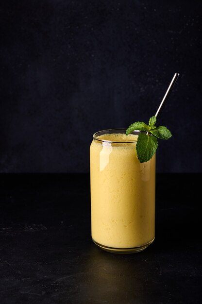 Orientacja pionowa mango lassi w szkle z rurką na ciemnym tle orientacja pionowa