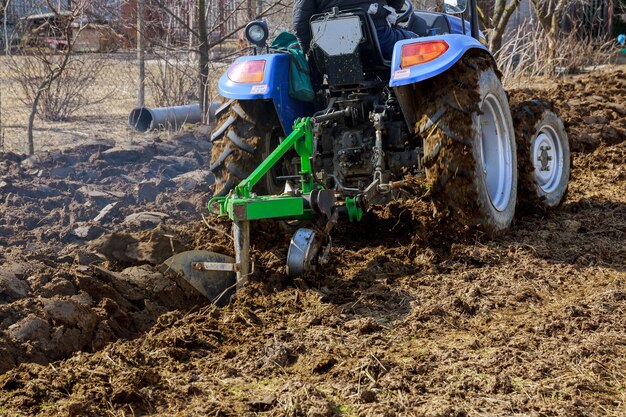 Orka pola. Mały traktor z osprzętem rolniczym uprawia ziemię.