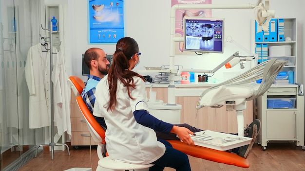 Ortodonta Omawia Badanie Rezonansu Magnetycznego Z Pacjentem Siedzącym Na Fotelu Stomatologicznym W Klinice Stomatologicznej. Kobieta Lekarz Wyjaśniająca Problem Stomatologiczny Mężczyźnie, Wskazując Cyfrowy Obraz Rentgenowski Przed Interwencją Dentysty