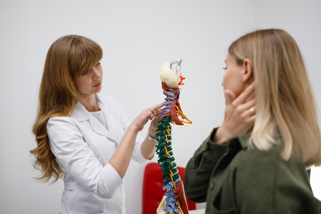 Zdjęcie ortopeda lub neurolog pokazuje pacjentce problematyczne obszary na modelu kręgosłupa