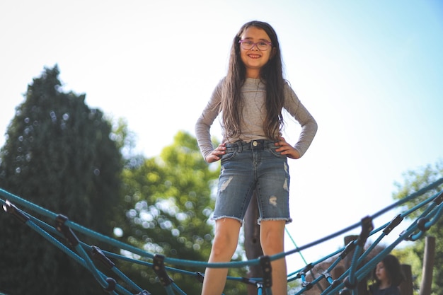 Osiemletnia kaukaska dziewczyna stoi na huśtawce z szczęśliwym uśmiechem w parku