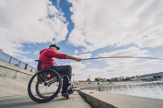 Osoba niepełnosprawna fizycznie na wózku inwalidzkim łowiąca z molo rybackiego