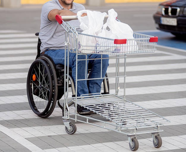 Osoba niepełnosprawna fizycznie pchająca wózek przed sobą na parkingu w supermarkecie