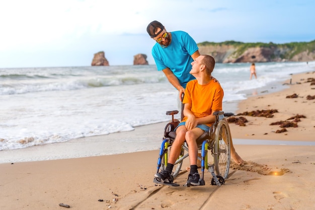 Osoba niepełnosprawna na wózku inwalidzkim na plaży popychana przez przyjaciół nad morzem cieszy się latem