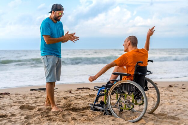 Osoba niepełnosprawna na wózku inwalidzkim na plaży z przyjacielem bawiącym się tańcem
