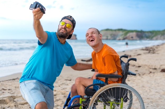 Osoba niepełnosprawna na wózku inwalidzkim na plaży z przyjacielem robiącym selfie