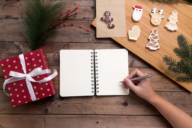 Osoba pisze na otwartym notatniku z pudełko i smaczne świąteczne ciasteczka domowej roboty