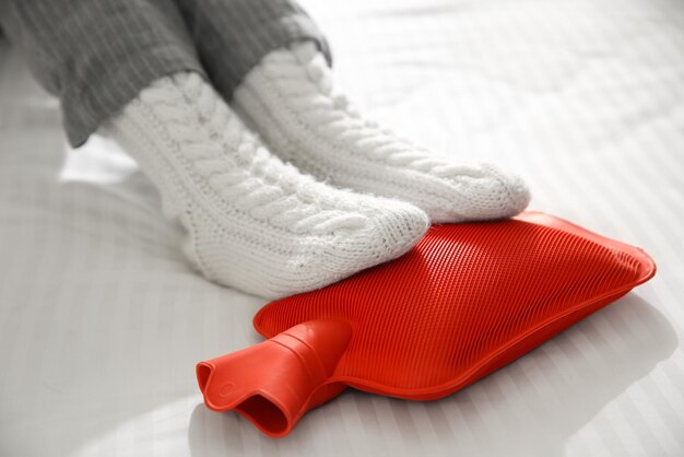 Osoba rozgrzewająca stopy butelką z gorącą wodą na zbliżeniu łóżka