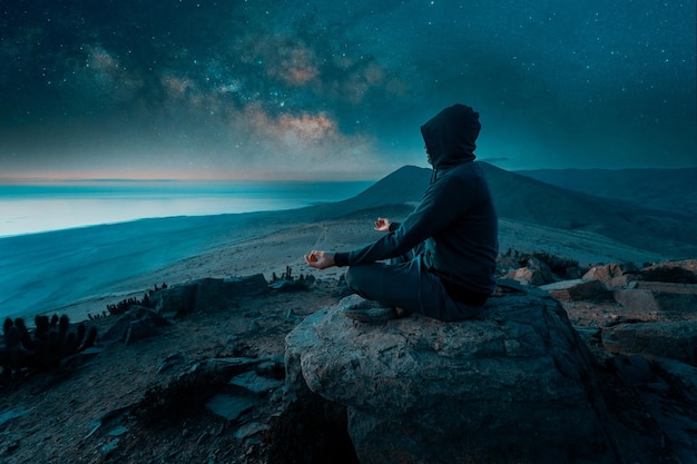 osoba siedząca na szczycie góry medytująca nocą nad oceanem