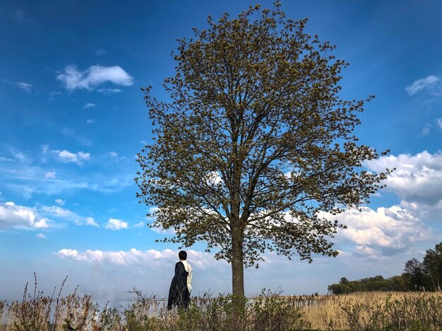 Zdjęcie osoba stojąca przy drzewie na polu przeciwko niebu