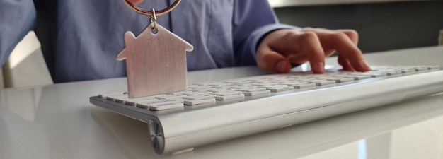 Osoba trzyma klucz do domu i brelok w kształcie domu na klawiaturze laptopa