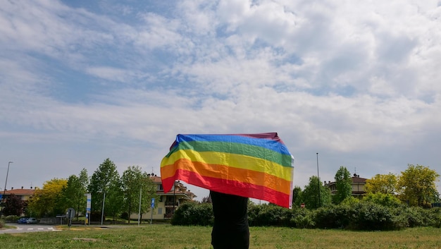 Zdjęcie osoba trzymająca flagę lgbt na tle nieba