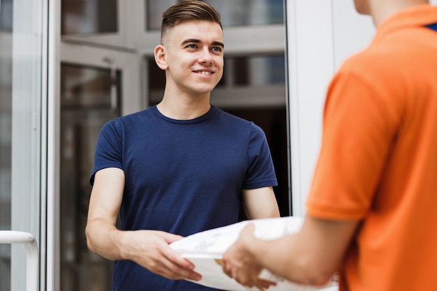 Zdjęcie osoba ubrana w pomarańczową koszulkę dostarcza przesyłkę do zadowolonego klienta. przyjazny pracownik, wysoka jakość usług dostawczych.