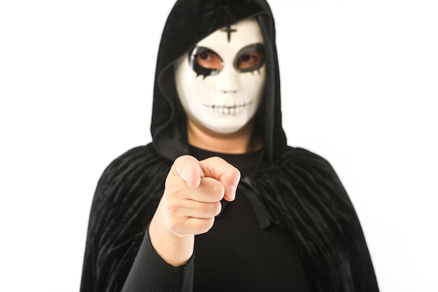 Osoba w białej masce z krzyżem na czole i czarnej aksamitnej pelerynie z nieostrym kapturem, wskazując na aparat z skoncentrowaną ręką, na białym tle. Koncepcja Karnawał, Halloween i Dzień Zmarłych.