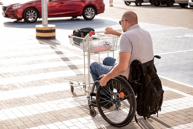 Zdjęcie osoba z niepełnosprawnością ruchową pcha wózek w kierunku samochodu na parkingu supermarketu