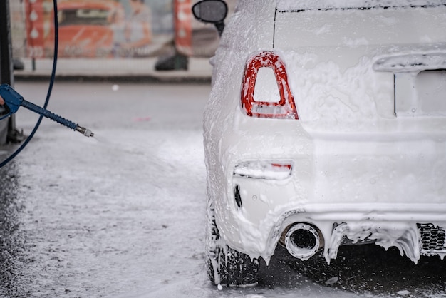 Osoba za sceną myje auto osobiste na myjni samoobsługowej z węża. Auto pokryte mydłem i wodą