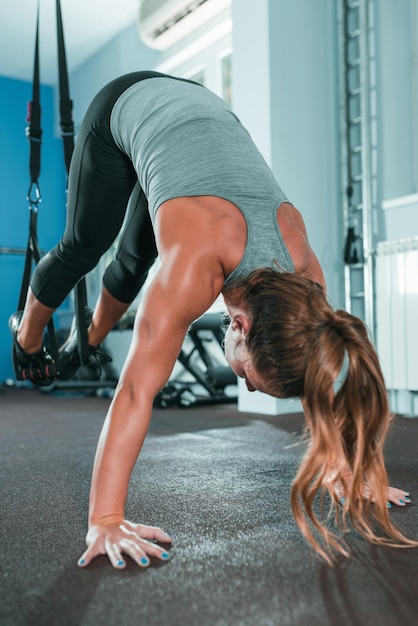 Osobisty trener ćwiczący na TRX z kobietą w siłowni