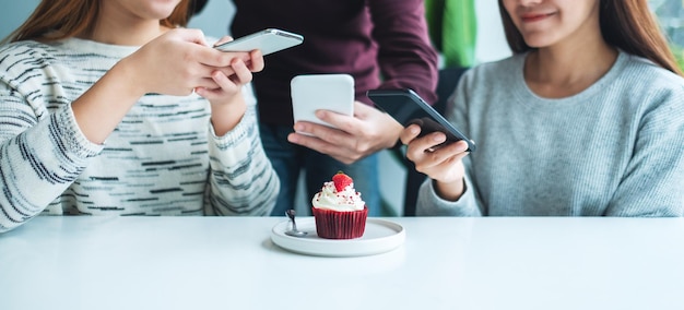 Osoby korzystające z telefonu komórkowego, aby zrobić zdjęcie babeczki przed jedzeniem w kawiarni