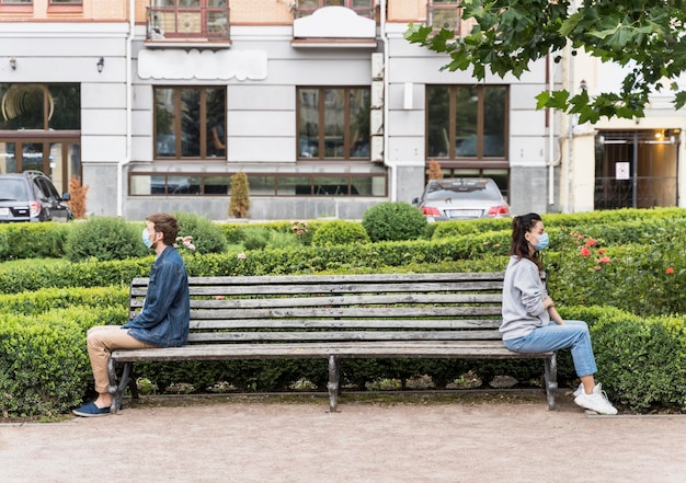 Osoby siedzące na ławce z dystansem, szanujące dystans społeczny