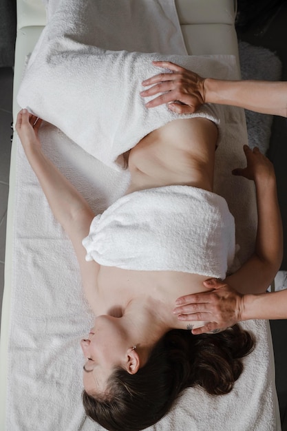 Osteopat naprawia leżącą kobietę na plecach ruchami rąk podczas wizyty w klinice terapii ręcznej