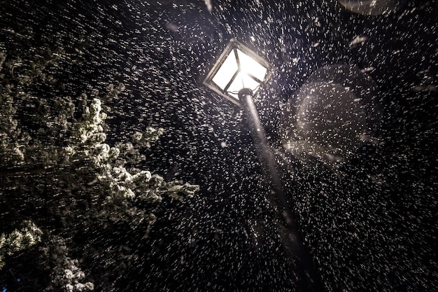 Oświetlona latarnia od dołu, gdy burza śnieżna spada w nocy