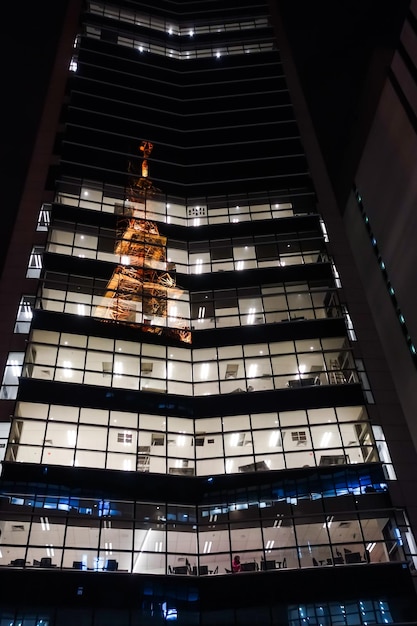 Oświetlona wieża odbita w oknach elewacji budynku w nocy