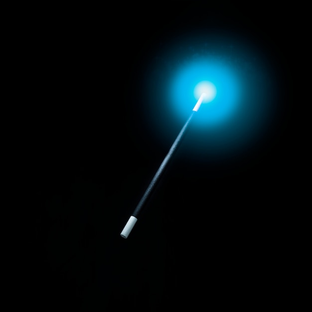 Zdjęcie oświetlone niebieskim świecącym światłem nad magiczną różdżką na czarnym tle