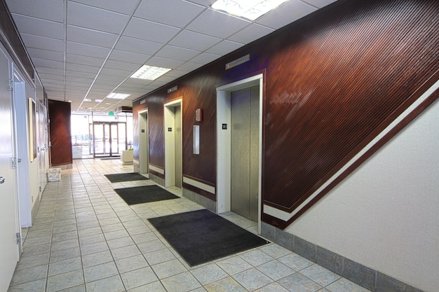 Oświetlony korytarz biurowy z windami i szklanymi drzwiami wyjściowymi