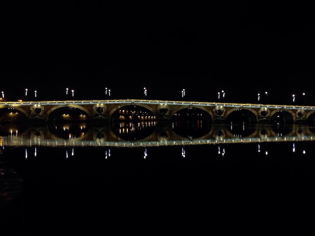 Zdjęcie oświetlony most łukowy odbijający się na spokojnej rzece na tle jasnego nieba w nocy