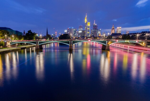 Zdjęcie oświetlony most nad rzeką przez budynki na tle nocnego nieba